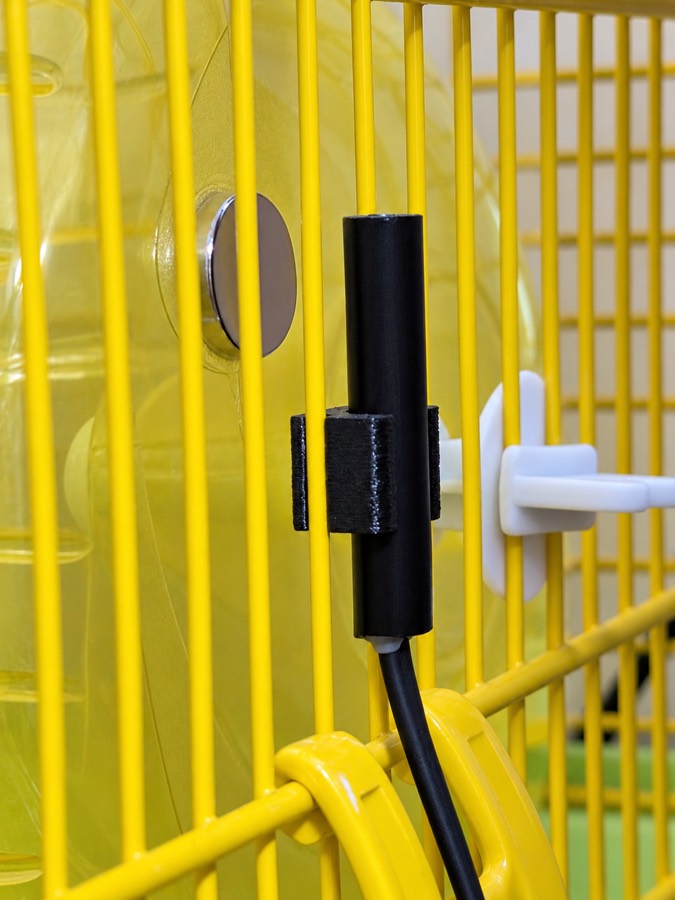 The sensor in its 3D-printed holder clipped to the cage bars, positioned close to the magnet on the wheel